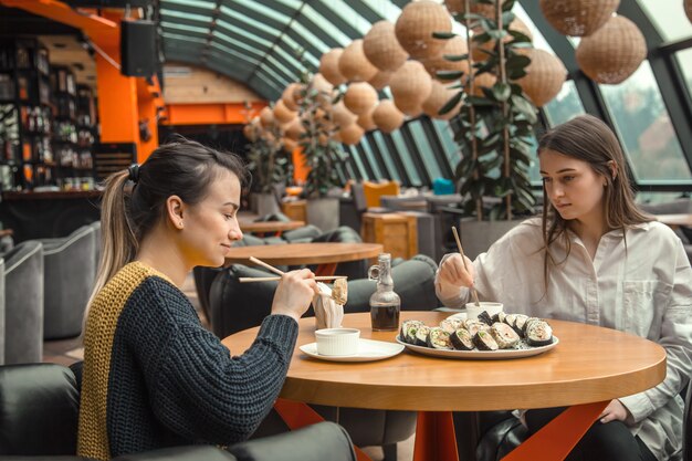 Due donne felici seduti in un caffè, mangiando sushi