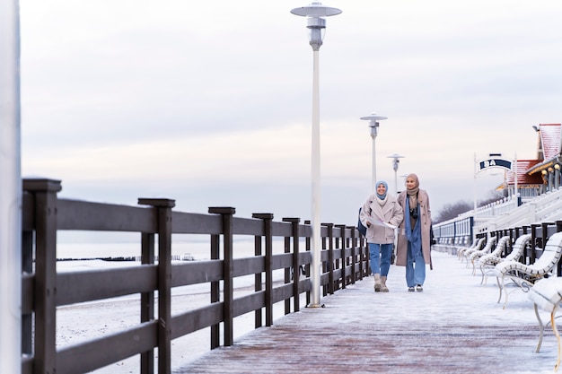 Due donne musulmane con l'hijab che consultano la mappa e camminano lungo l'oceano mentre viaggiano