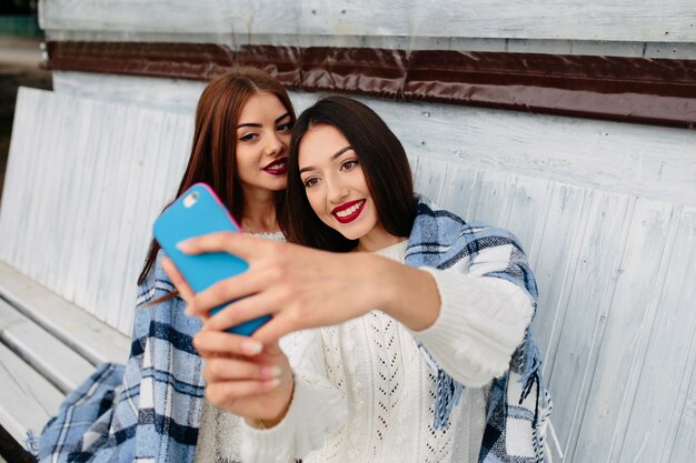 Due donne si siedono in panchina e fanno selfie