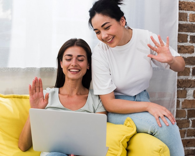 Due donne sul divano in chat video e agitando il computer portatile