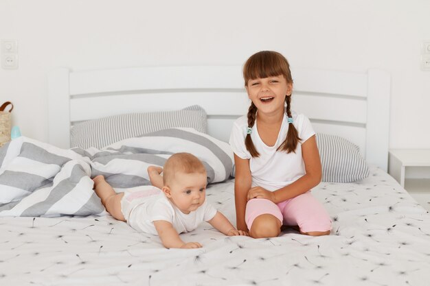 Due fratelli che giocano a casa, in posa sul letto, un bambino più grande che sorride direttamente alla telecamera, un bambino più anziano dai capelli scuri che indossa uno stile casual che gioca con un bambino sdraiato sulla pancia.