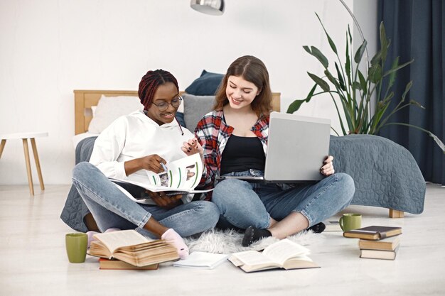 Due giovani adolescenti che si siedono su un pavimento vicino al letto studiando e usando un computer portatile