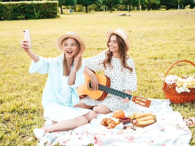 Due giovani bella donna hipster in prendisole e cappelli estivi alla moda. Donne spensierate che fanno picnic all'esterno.