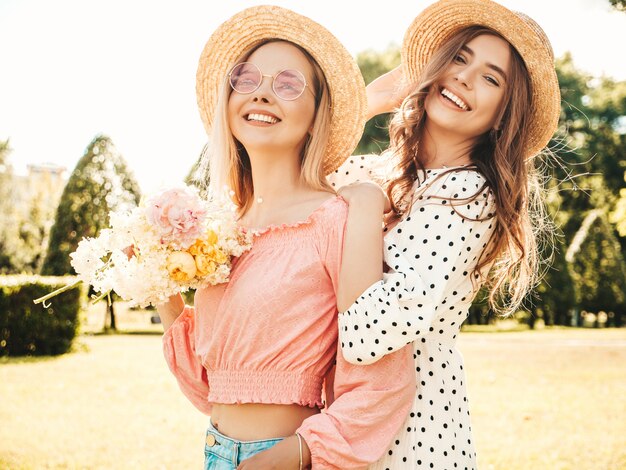 Due giovani bella donna sorridente hipster in prendisole estive alla moda. Donne spensierate sexy che posano nel parco in cappelli.