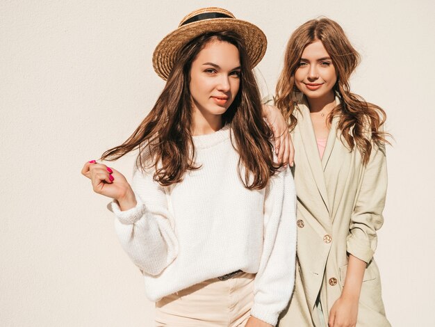 Due giovani belle donne hipster sorridenti in maglione e cappotto bianchi alla moda