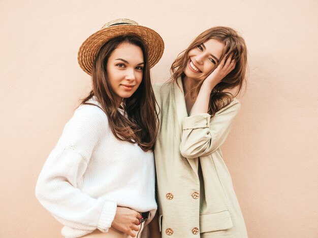 Due giovani belle donne hipster sorridenti in maglione e cappotto bianchi alla moda