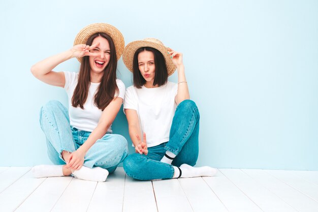 Due giovani belle donne hipster sorridenti in t-shirt bianca estiva alla moda e vestiti di jeans