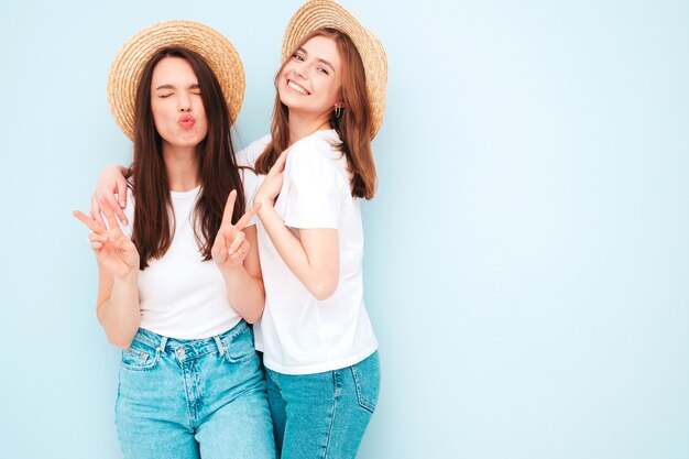 Due giovani belle donne hipster sorridenti in t-shirt bianca estiva alla moda e vestiti di jeans