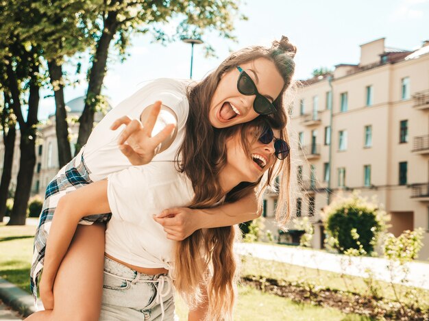 Due giovani belle donne hipster sorridenti in vestiti di t-shirt bianca estiva alla moda