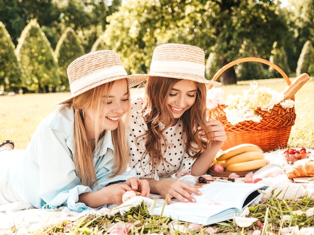 Due giovani belle donne sorridenti in prendisole e cappelli estivi alla moda. Donne spensierate che fanno picnic all'esterno.