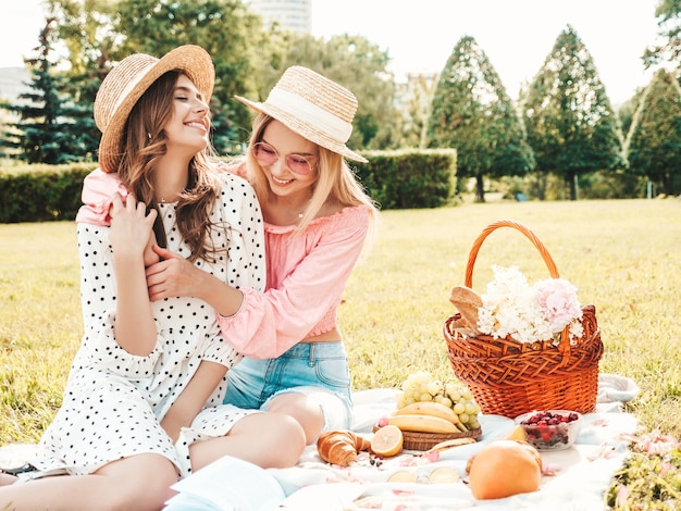 Due giovani belle donne sorridenti in prendisole e cappelli estivi alla moda. Donne spensierate che fanno picnic all'esterno.