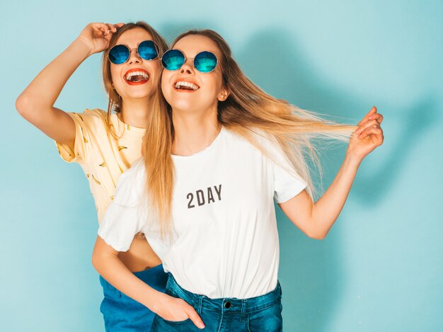 Due giovani belle ragazze bionde sorridenti dei pantaloni a vita bassa in gonne d'avanguardia dei jeans dell'estate vestiti.