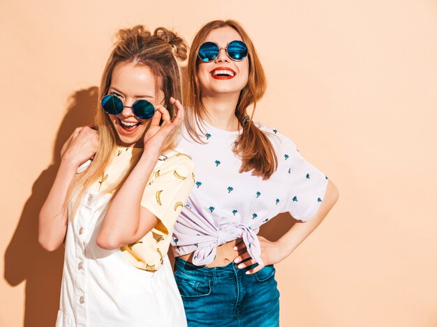 Due giovani belle ragazze bionde sorridenti dei pantaloni a vita bassa in vestiti variopinti della maglietta di estate alla moda.