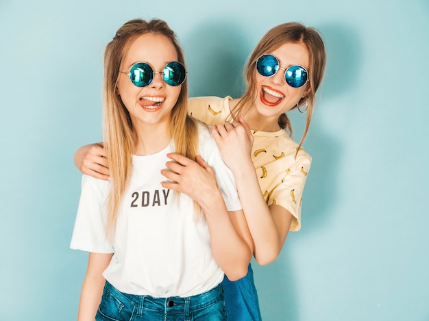 Due giovani belle ragazze bionde sorridenti dei pantaloni a vita bassa in vestiti variopinti di estate d'avanguardia.