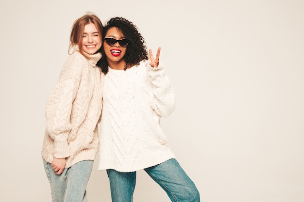 Due giovani belle ragazze sorridenti hipster in maglioni invernali alla moda. Modelli positivi che si divertono e si abbracciano