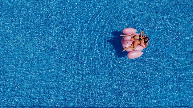 Due giovani donne felici con figure nuotano in piscina per i fenicotteri. Vista dall'alto.