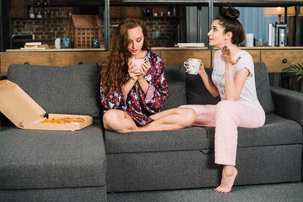 Due giovani donne sedute sul divano facendo colazione