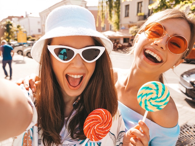 Due giovani donne sorridenti dei pantaloni a vita bassa in vestiti casuali di estate.