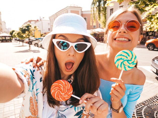 Due giovani donne sorridenti dei pantaloni a vita bassa in vestiti casuali di estate.