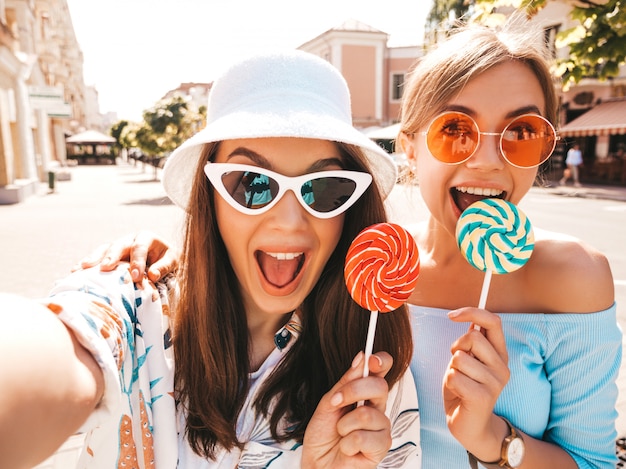 Due giovani donne sorridenti dei pantaloni a vita bassa in vestiti casuali di estate.