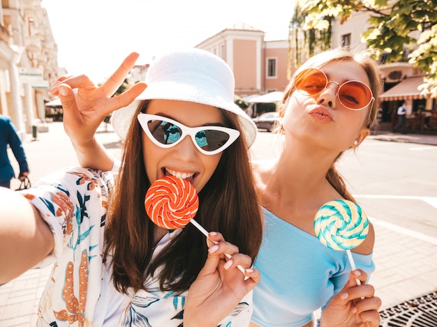 Due giovani donne sorridenti dei pantaloni a vita bassa in vestiti casuali di estate.