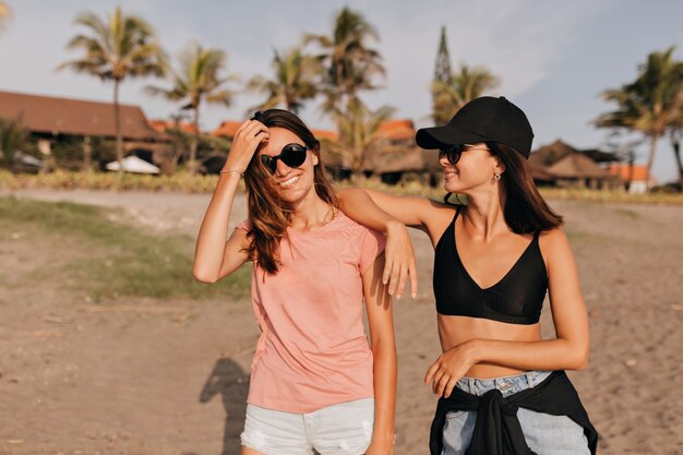 Due giovani donne sulla spiaggia divertendosi sentono la libertà sull'oceano riva nella soleggiata giornata estiva Le amiche che godono delle vacanze al mare