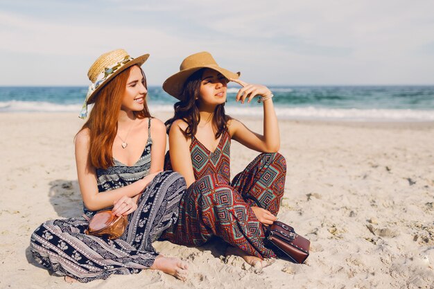 Due giovani donne sveglie che si siedono sulla spiaggia