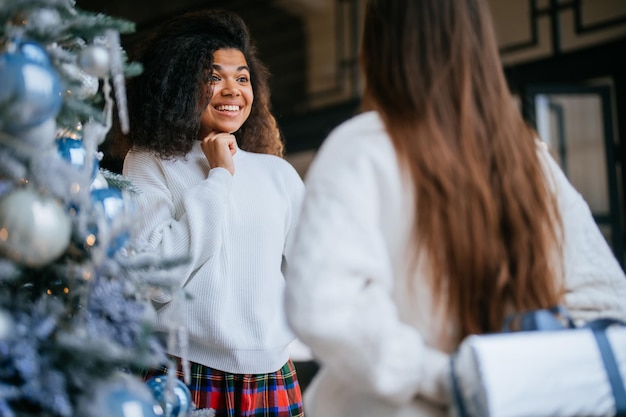 Due giovani e felici migliori amici compagni di stanza davanti a un albero di Natale si scambiano i regali per le vacanze di Capodanno. Concetto di vacanze