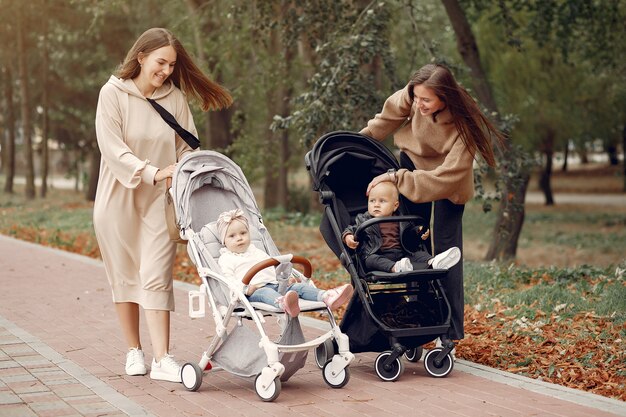 Due giovani madri che camminano in un parco in autunno con le carrozze