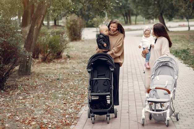 Due giovani madri che camminano in un parco in autunno con le carrozze