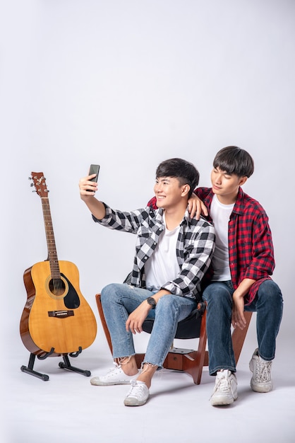 Due giovani uomini amorevoli si siedono su una sedia e prendono un selfie da uno smartphone.