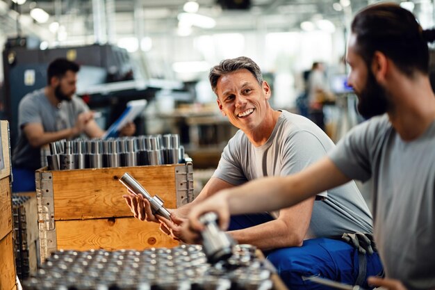 Due lavoratori siderurgici felici che preparano prodotti per la distribuzione e comunicano in una struttura industriale Il focus è sul lavoratore di mezza età