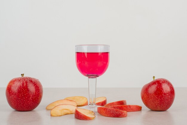 Due mele rosse, fette di mela e un bicchiere di limonata.