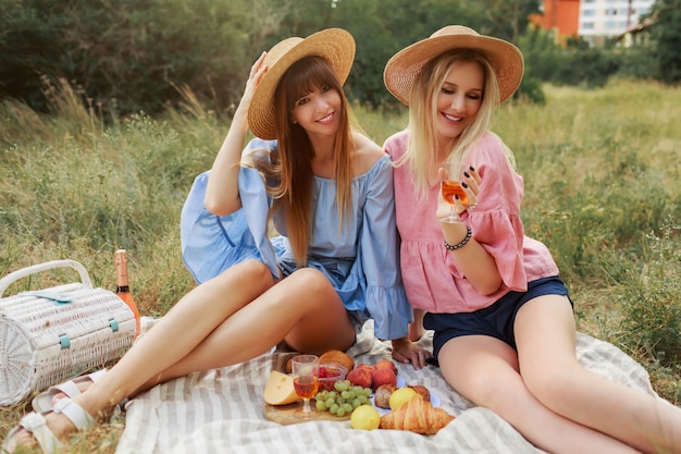 Due meravigliose ragazze in cappello di paglia che trascorrono le vacanze in campagna, bevendo spumante.