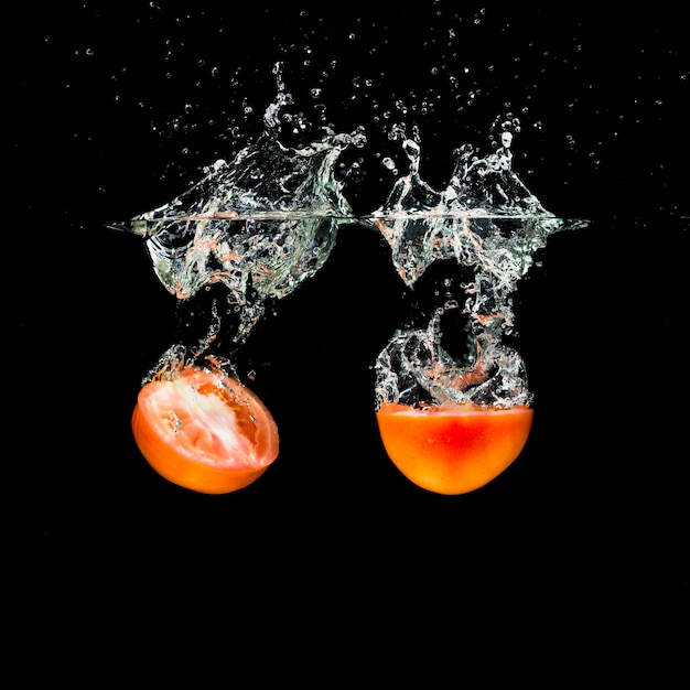 Due metà pomodori che si tuffano in acqua pulita