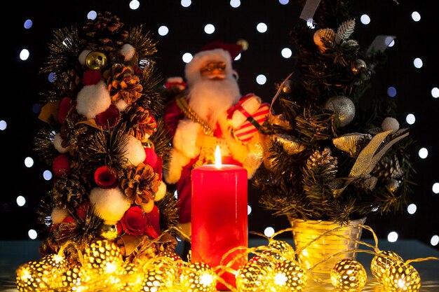 Due mini alberi di natale e una statuetta di babbo natale su sfondo nero con luci bokeh su di esso