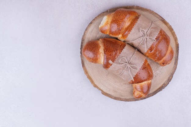 Due panini croissant in involucro di carta su tavola di legno.