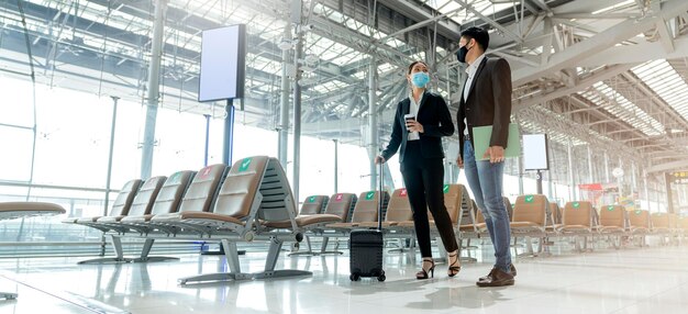Due partner commerciali asiatici con protezione della maschera facciale distanza sociale nuovo stile di vita normale I viaggiatori d'affari che camminano in aeroporto con i bagagli