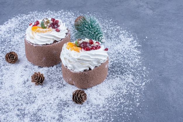 Due pasticcini cremosi con zucchero in polvere e pigne di Natale