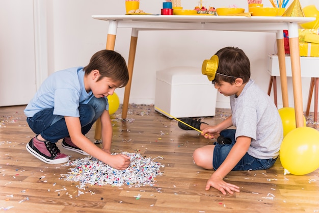 Due piccoli amici che riuniscono i coriandoli sul pavimento nella festa