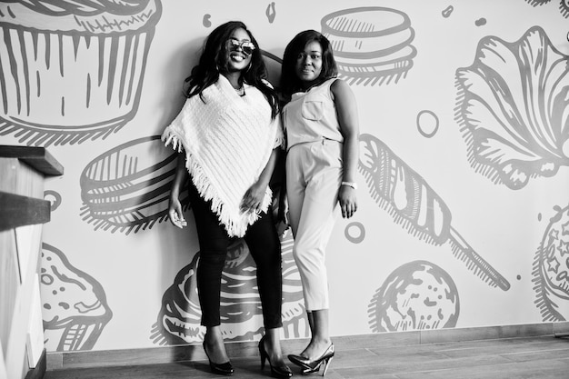 Due ragazze afroamericane alla moda al caffè poste contro il muro
