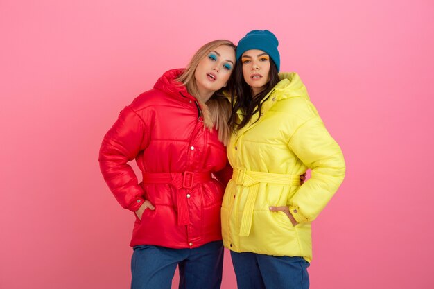 Due ragazze attraenti in posa su sfondo rosa in piumino invernale colorato di colore rosso e giallo brillante