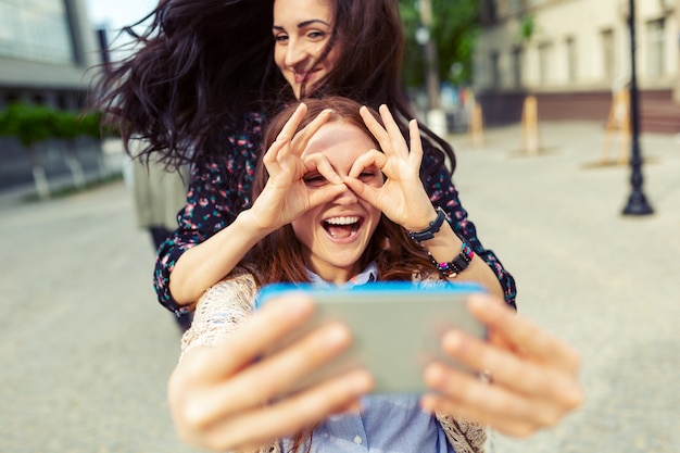 Due ragazze che fanno selfie divertenti per strada, divertendosi insieme