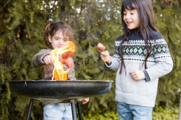 Due ragazze che preparano salsicce sul barbecue in fiamme all&#39;aperto