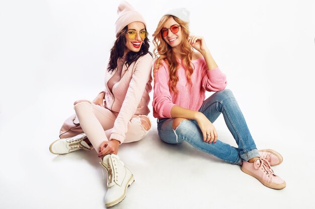 Due ragazze che ridono, migliori amiche in posa in studio su sfondo bianco. Abito invernale rosa alla moda.