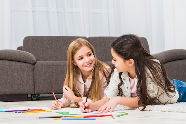 Due ragazze che si trovano sul tappeto che disegna con le matite di colore nel salone