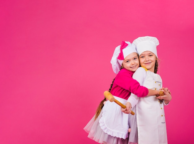 Due ragazze cuochi con gli utensili della cucina che abbracciano