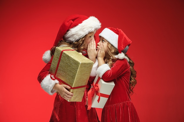 Due ragazze felici in cappelli di babbo natale con scatole regalo su rosso