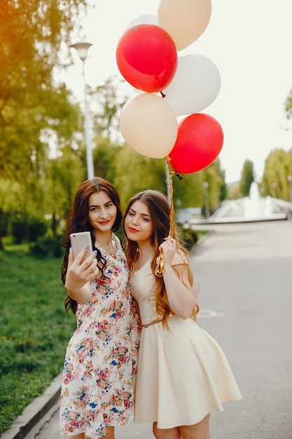 due ragazze giovani e luminose passano il loro tempo nel parco estivo con palloncini e telefono