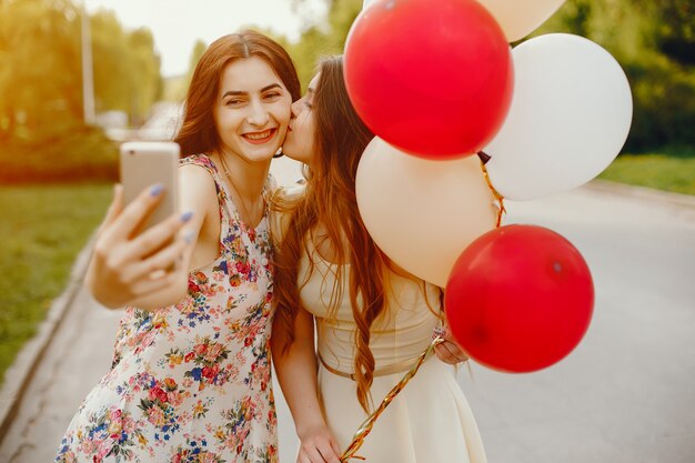 due ragazze giovani e luminose passano il loro tempo nel parco estivo con palloncini e telefono